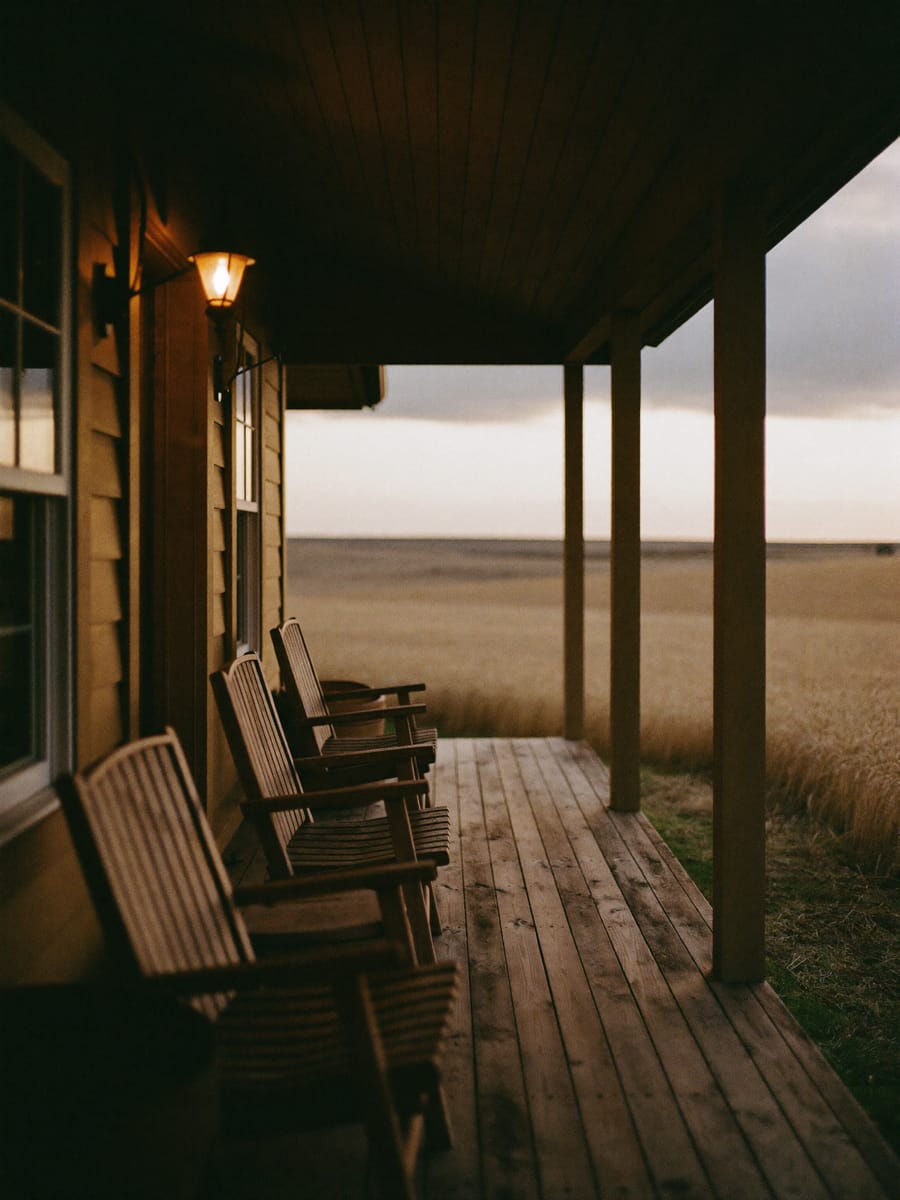 A farmhouse porch with chairs looking over wheat fields at dusk