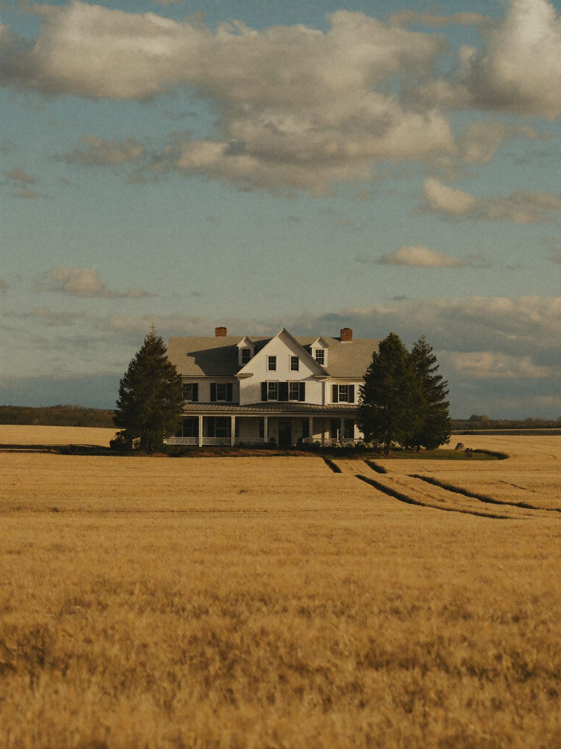 A classic acreage home with a wide porch beyond a golden wheat field