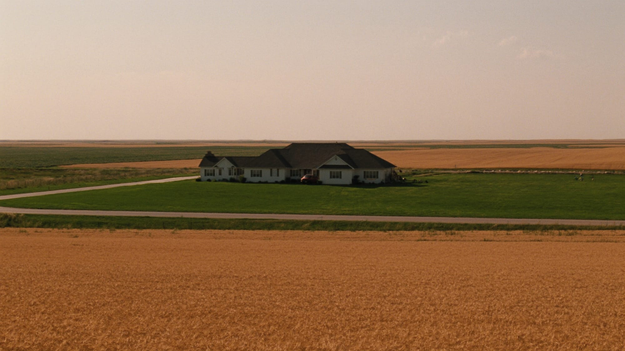 A well-kept acreage home with a wide lawn beside golden wheat fields on the flat Peace Country prairie