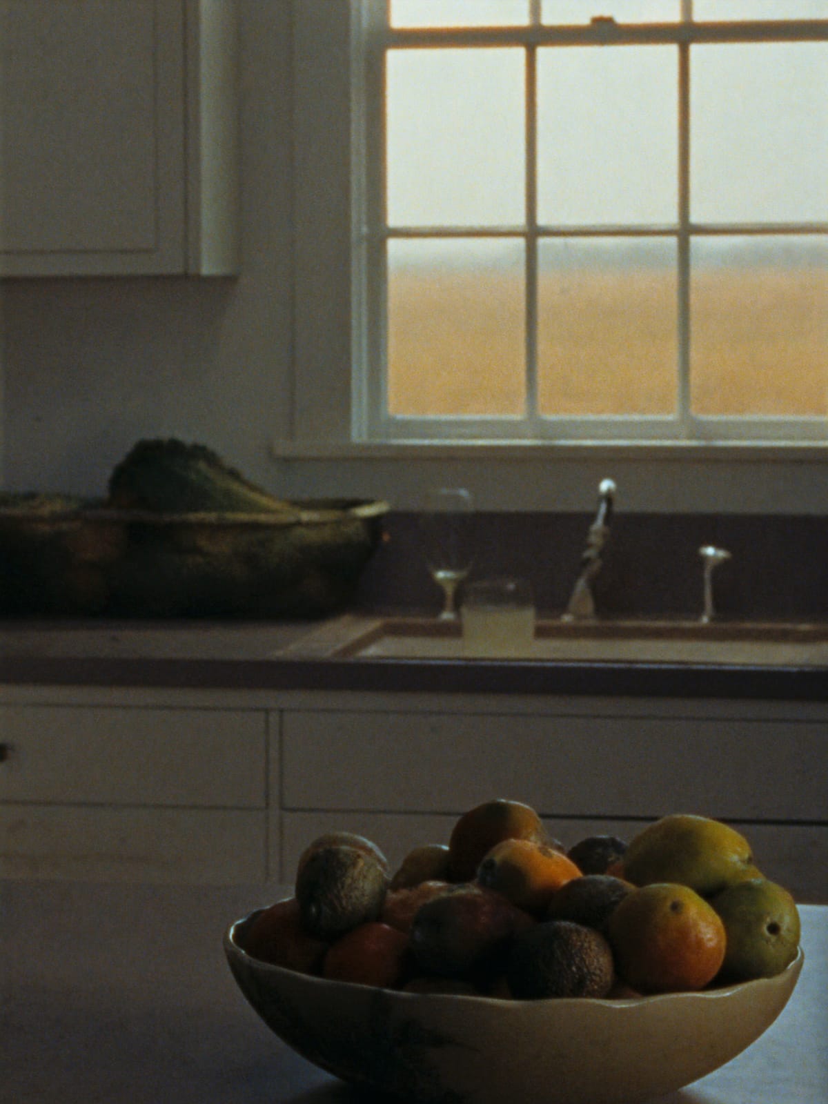 A farmhouse kitchen with a bowl of fruit and prairie light through the window over the sink